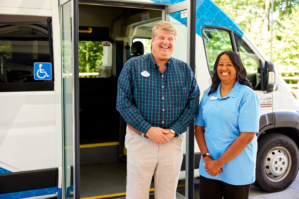 Two team members in front of an activities bus, happy with their careers in senior living