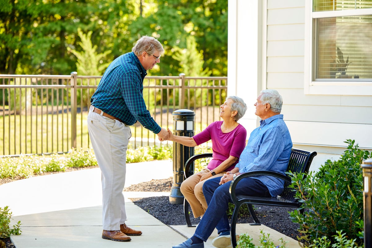 Arbor team member greets two residents sitting in a beautifully landscaped area