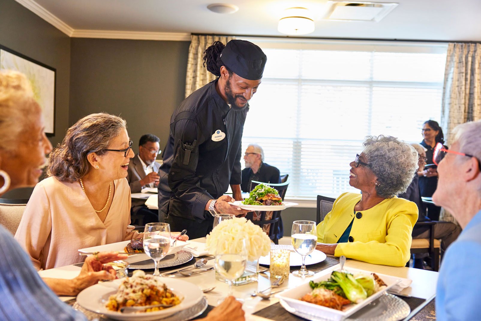 Server working in assisted living community places beautiful entree on dining table