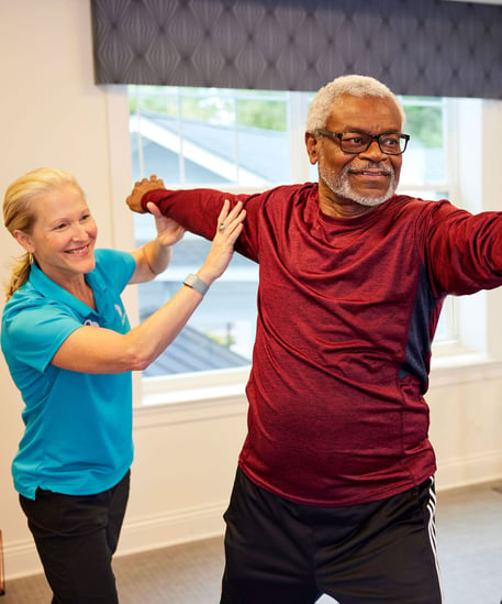A happy engagement coordinator with a senior living career helps a resident stretch