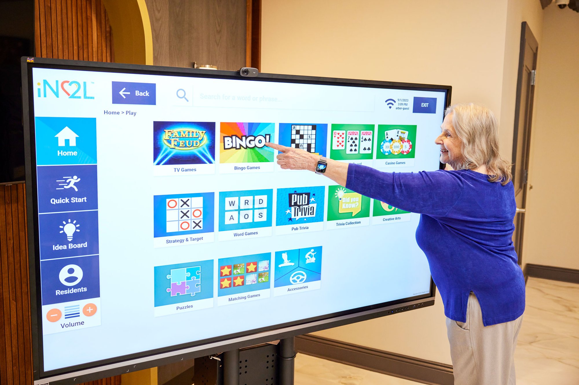 A member of the engagement team in front of a large screen selecting the Bingo game for residents to play