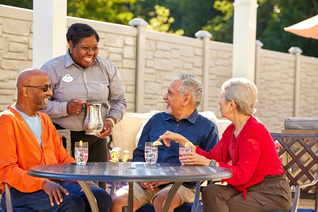 Smiling server pours water for 3 residents Arbor senior residents sitting outside