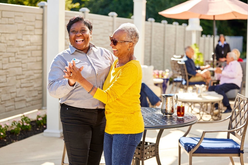 Arbor resident and team member smile and dance in an outdoor dining space