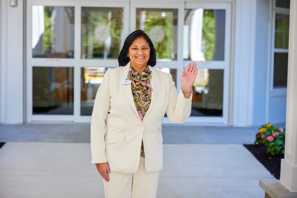 Smiling administrative team member waving from the front of an Arbor community